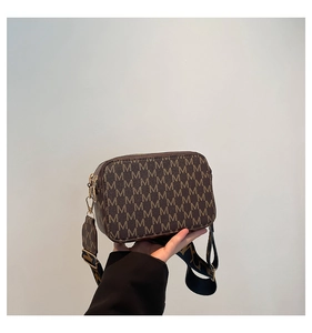 Detail of a brown monogram camera bag with a wide colorful fabric strap and gold hardware