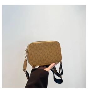Detail of tan camera bag featuring M-monogram pattern and adjustable wide fabric strap
