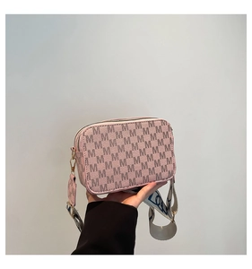 Close-up of pink camera bag with monogram texture and wide patterned fabric strap