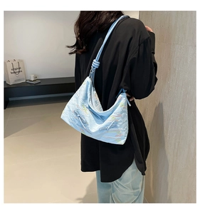 Close-up of light blue pleated tote bag with wave embroidery on a shoulder strap model