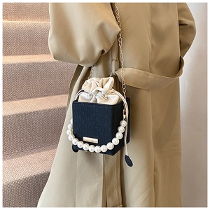 Dettaglio borsa a scatola nera con perle e catena indossata su un trench coat beige