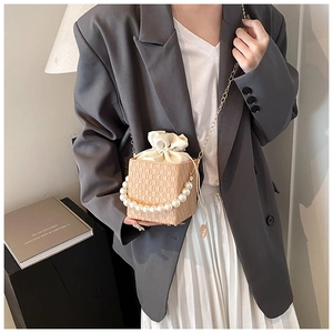 Dettaglio della borsa intrecciata beige con manico di perle e catena dorata
