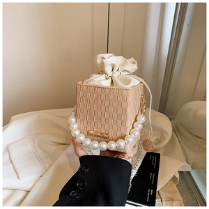 Dettaglio borsa a cubo intrecciata beige con manico di perle e sacchetto interno in raso