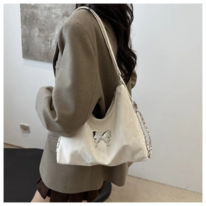 Détail d'un sac à bandoulière blanc avec papillon argenté et texture de cuir