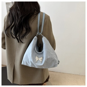 Détail du sac hobo bleu clair avec papillon métallique et texture plissée à l'épaule