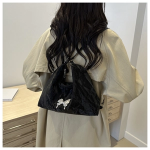 Détail du sac plissé noir avec papillon argenté porté sur un trench-coat kaki