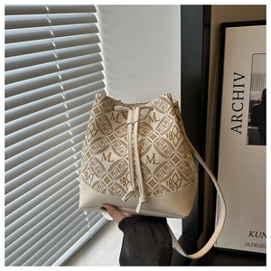 Detail of minimalist cream drawstring bucket bag featuring brown monogram print and leather trim
