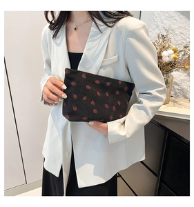 Détail d'un sac à main en velours côtelé noir avec motif fraise tenu par un mannequin