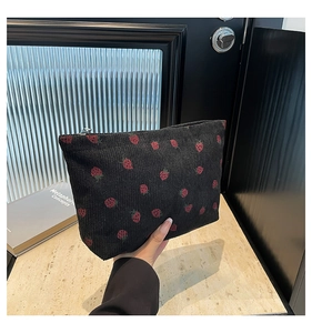 Dettaglio di una trousse in velluto a coste nero con stampa di fragole