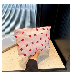 Dettaglio della borsa in velluto rosa con stampa fragole tenuta in mano per le dimensioni