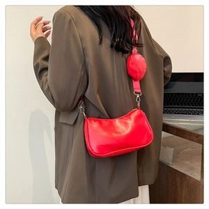 Detail of red baguette bag with wide strap and round coin purse charm on a model