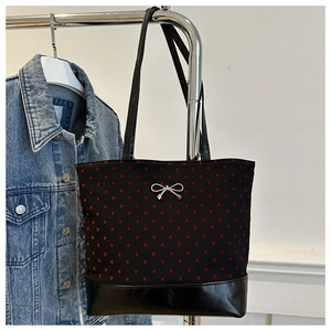 Detail of black heart canvas tote bag featuring silver bow charm and shiny leather base