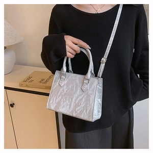 Detail of silver pleated tote bag with dual handles and adjustable strap in a modern setting