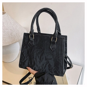 Detail of black pleated texture handbag with gold hardware and removable shoulder strap