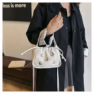 Dettaglio borsa a secchiello in velluto bianco con coulisse e farfalle in bronzo