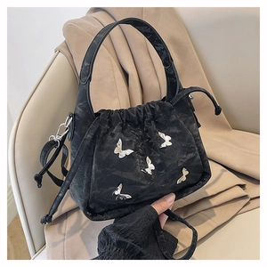 Detail of black pleated crossbody bag with silver butterfly charms on beige blazer