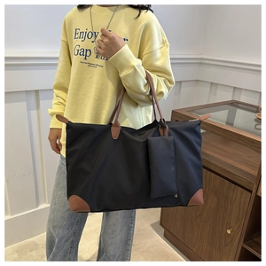 Detail of black nylon tote bag with brown leather handles and small attached pouch