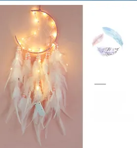 Detail of pink moon dreamcatcher with white feathers and warm LED fairy light glow