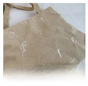 Close-up of khaki corduroy tote bag texture with white embroidered letters and text