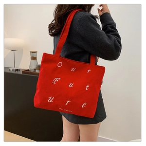 Close-up of a red corduroy tote bag featuring white embroidered Our Future slogan text