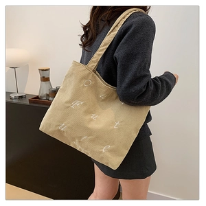 Detail of light beige corduroy tote bag featuring artistic white letter embroidery