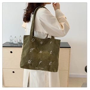 Detail of dark green corduroy tote bag with Our Future embroidery worn over shoulder
