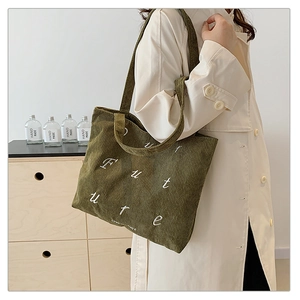 Close-up of olive green corduroy tote bag with Future embroidery on white trench coat