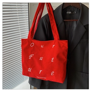 Close-up of red corduroy tote bag featuring white Our Future embroidery on black suit