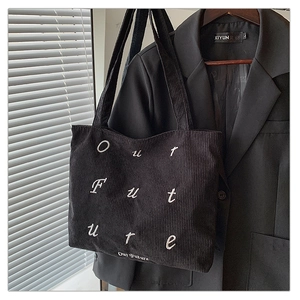 Close-up of black corduroy tote bag featuring white embroidered Our Future lettering