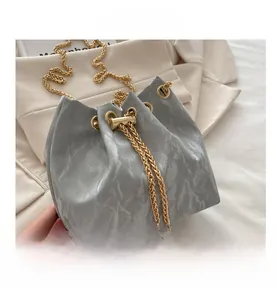 Detail of silver bucket bag with wrinkled texture and golden chain strap on fabric