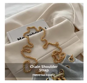 Detail of golden woven metal chain strap on minimalist grey leather shoulder bucket bag