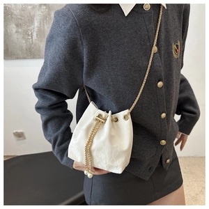 Detail of white drawstring bucket bag with gold chain strap and pearl accents