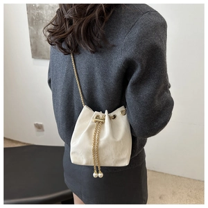 Détail du sac seau blanc cassé avec cordon de serrage, chaîne dorée et perles élégantes