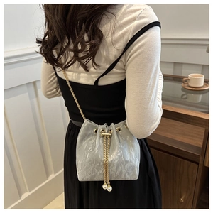 Détail du sac seau gris avec cordon à perles et chaîne dorée porté par un mannequin