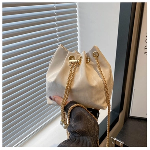 Détail du sac seau crème avec cordon de serrage, chaîne dorée et glands en perles
