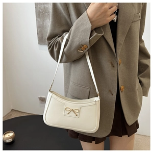 Close-up of off-white baguette bag featuring a golden metal bow buckle and matte leather