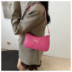 Detail of fuchsia underarm bag with elegant gold bow hardware and leather texture