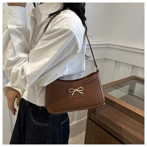 Detail of brown faux leather baguette bag with a stylish gold bow buckle on a model