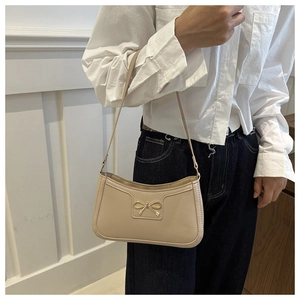 Detail shot of a beige leather underarm bag featuring a golden metal bow accessory