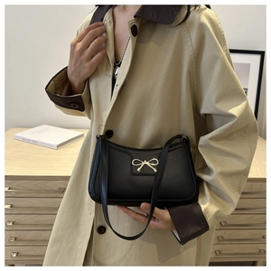Detail of a chic black underarm bag with a golden bow ornament worn over a khaki trench coat