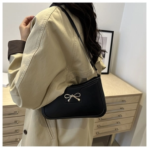 Detail of black leather underarm bag with gold bow on model in beige trench coat