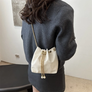 Sac seau beige minimaliste avec chaîne dorée et détails perlés porté par un modèle