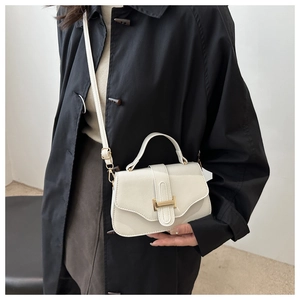 Detail view of white leather crossbody bag with gold T-shaped buckle on black coat