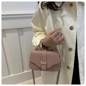 Close-up of dusty pink leather shoulder bag with gold clasp on model in beige coat