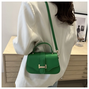 Detail of green leather handbag with golden H-clasp worn as a crossbody bag