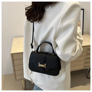 Detail of a black pebbled leather underarm bag with a golden H buckle on a white blazer