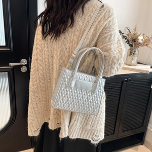 Silver quilted crossbody bag with metallic finish and circular handles on a model