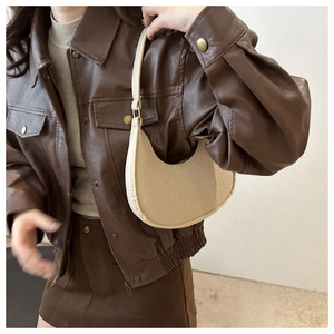 Detail of beige faux crocodile leather underarm bag worn by model over a brown jacket