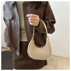 Close-up of cream crescent shoulder bag with crocodile texture on brown leather outfit