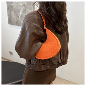 Detail showing bright orange crescent underarm bag with elegant crocodile texture